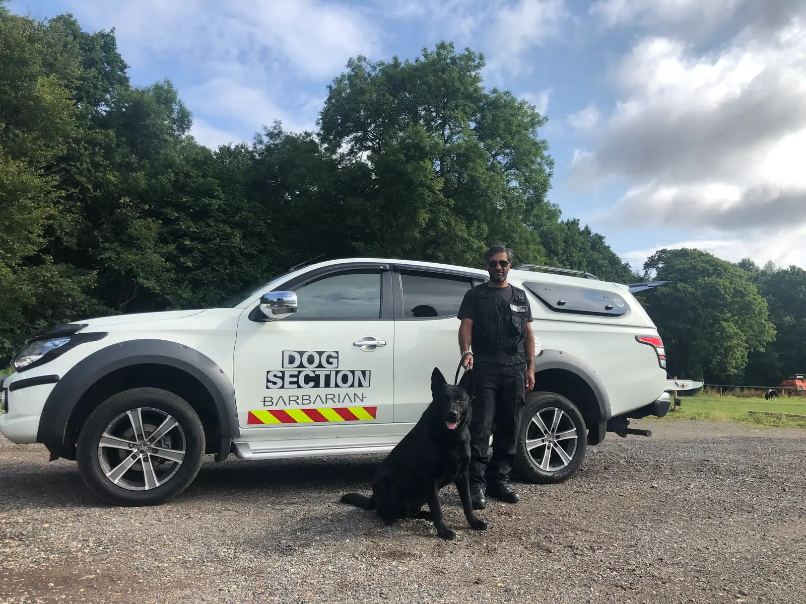 Dog handler with a German Shepherd beside a dog section patrol vehicle