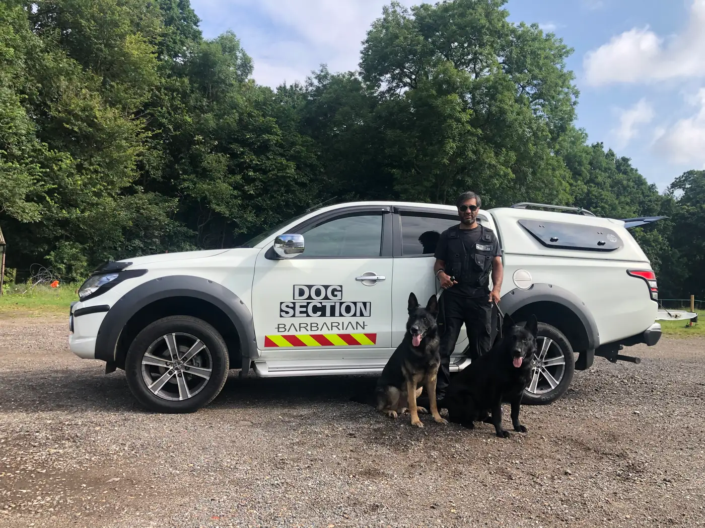 Dog handler with two German Shepherds beside a dog section patrol vehicle